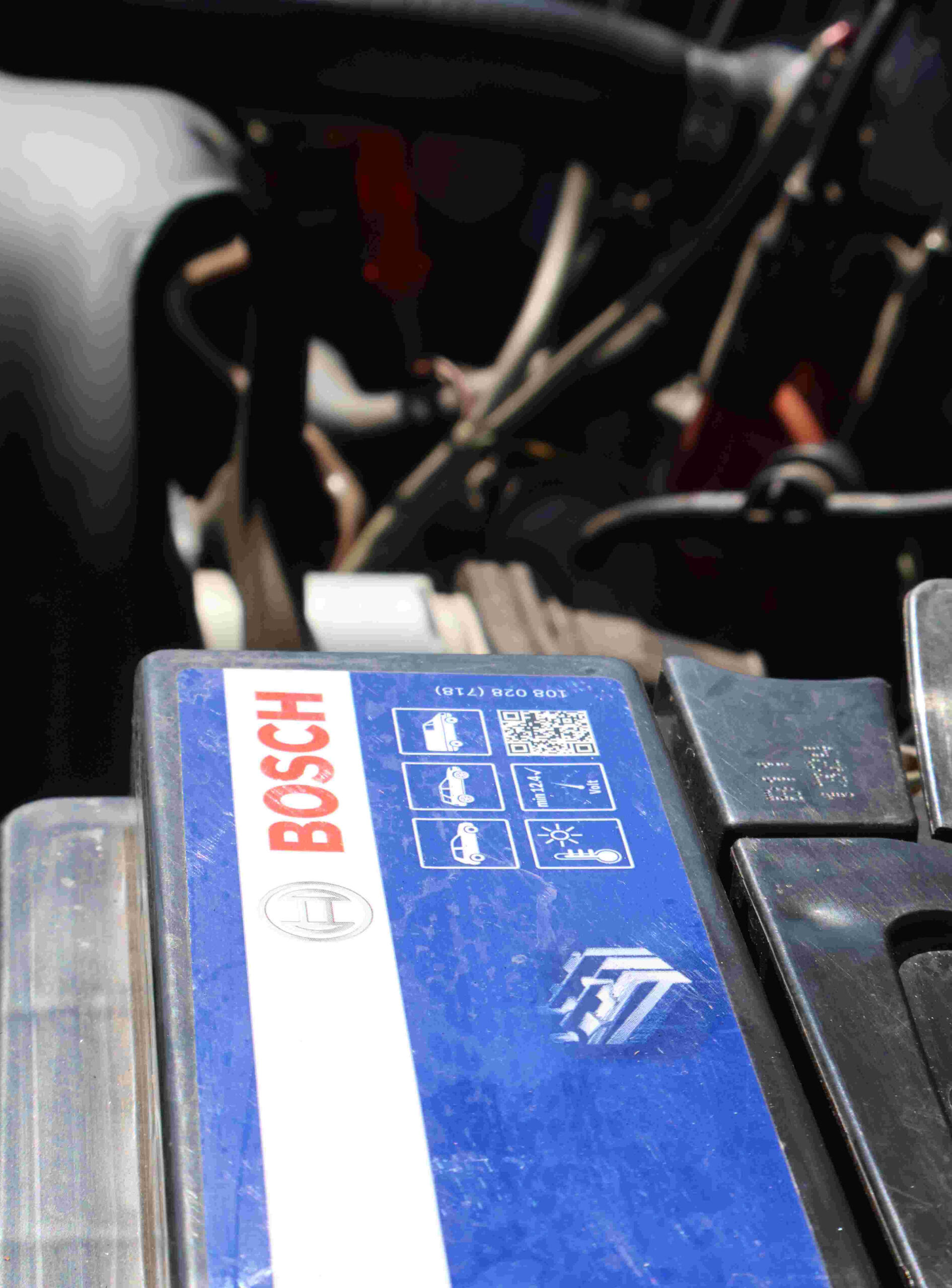 Bosch car battery with a blue sticker, saying "BOSCH" in red writing, battery placed inside of a vehicle.